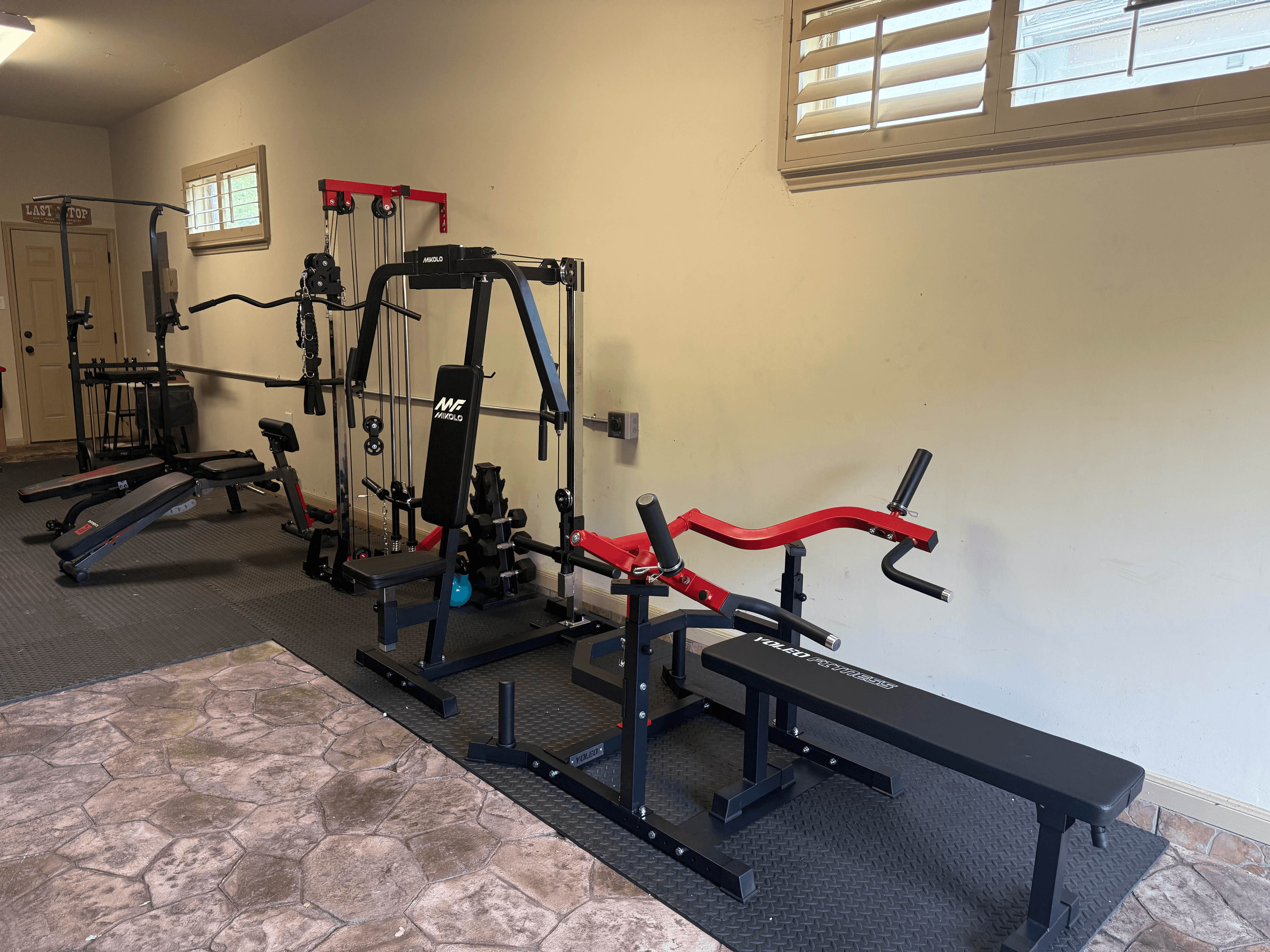 Black and red home gym equipment, including cable machines and benches, organized on rubber mats.