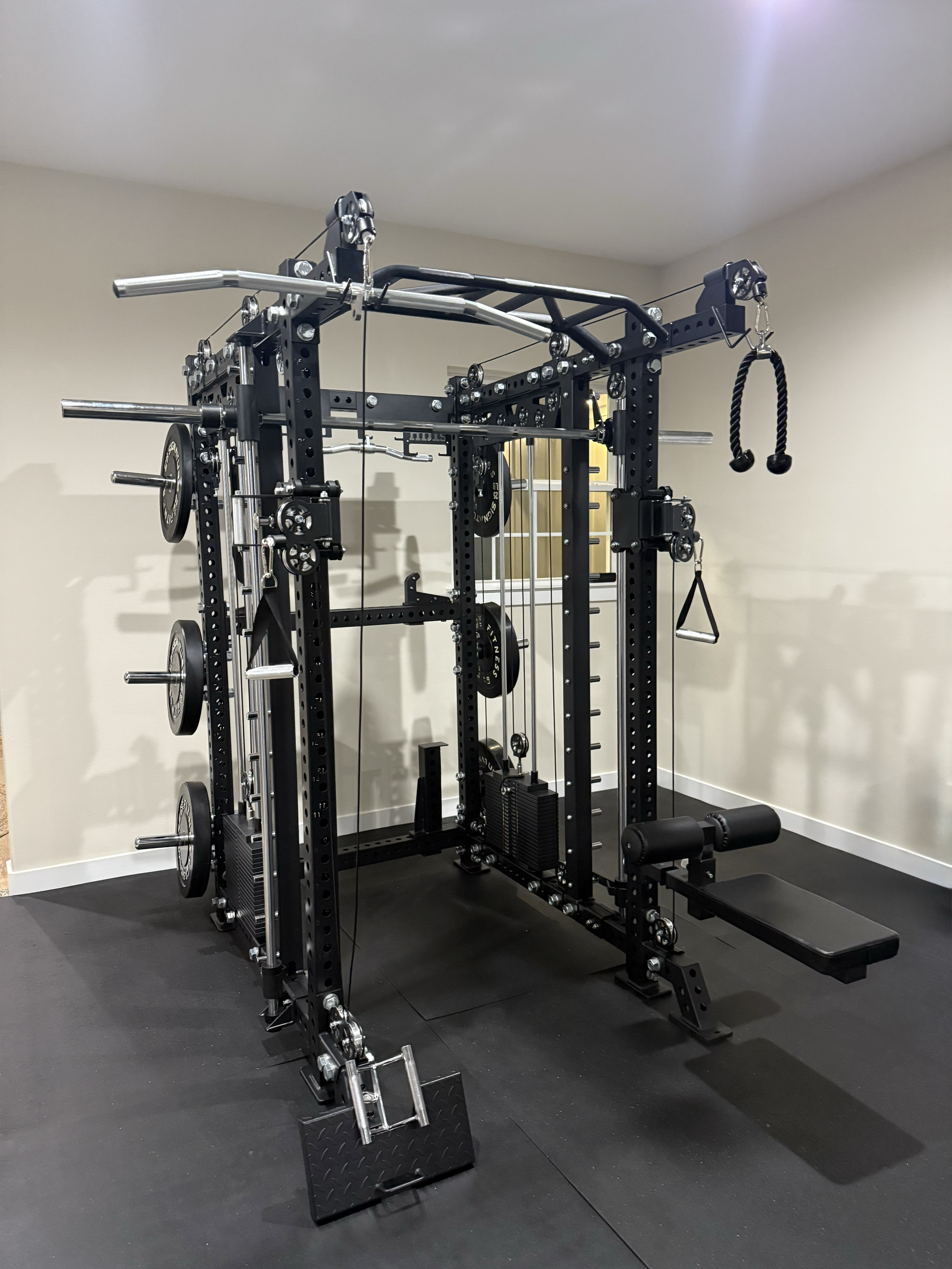 Black multi-functional home gym power rack with cable pulleys, weight plates, and a bench.